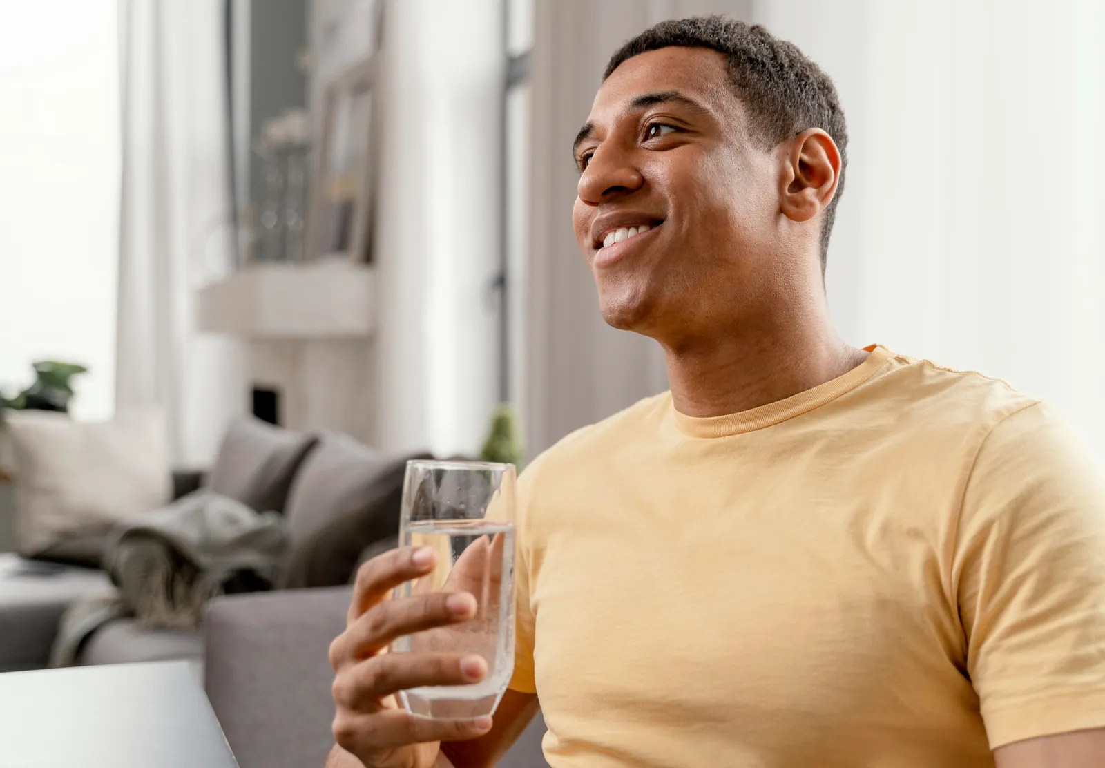 Homme souriant buvant un verre d'eau pure à la maison